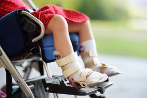 Disabled girl sitting in wheelchair. On her legs orthopedic equipment . Child cerebral palsy. Inclusion.